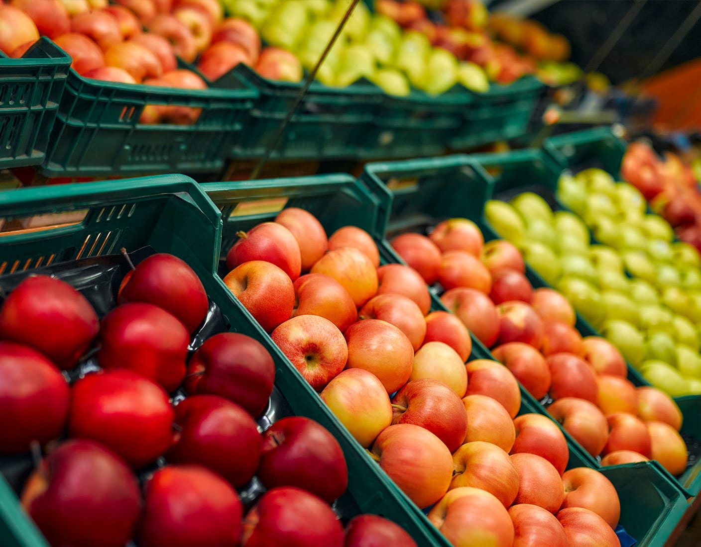 Rows of red, pink, and green apples displayed in black crates at a market.